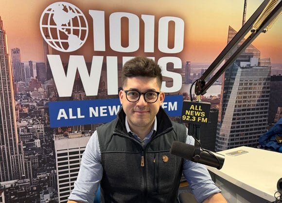 Photo of an individual speaking into a microphone at a radio station.