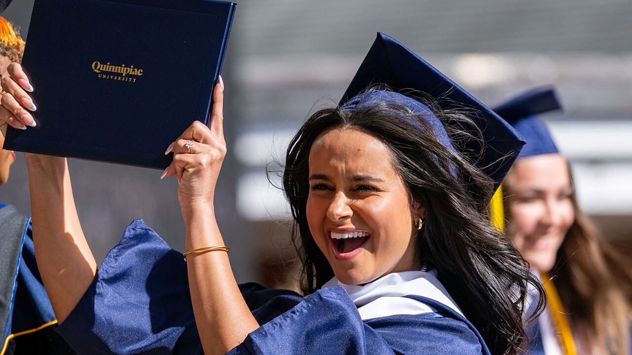 A graduate walks off stage excitedly holding up her diploma